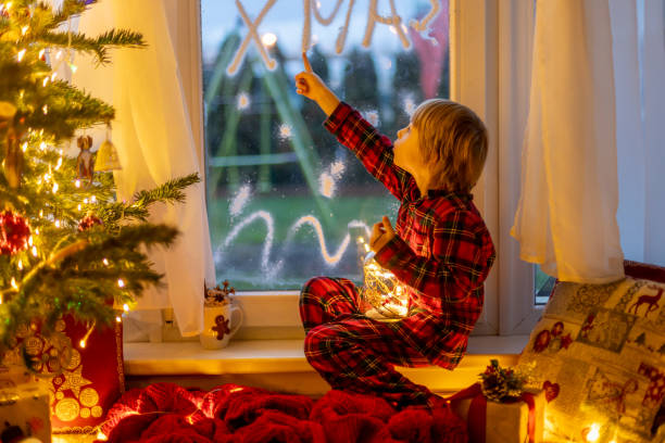 istock Cute child, sitting on a window, looking outdoors for Santa Claus 1962102291