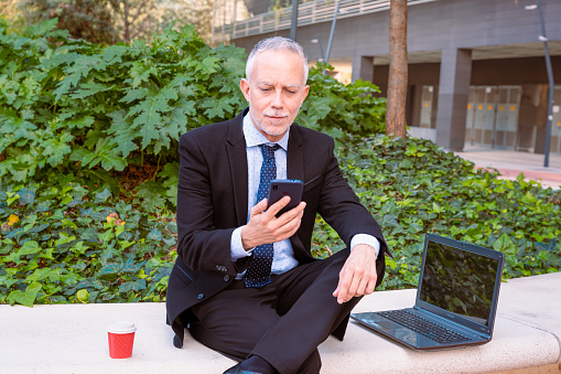 Mid adult man in a suit holds a phone in his hands, writes messages and reads news online, using an application