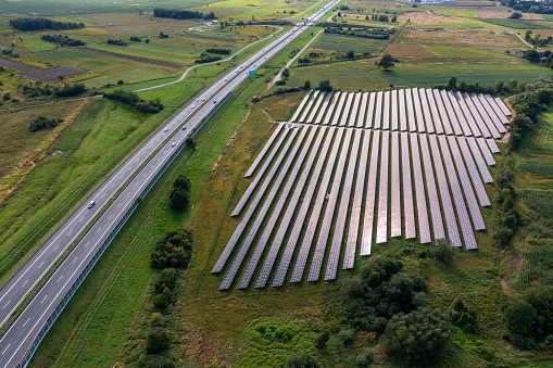 Aerial view of a new solar power plant next to the highway among green fields.