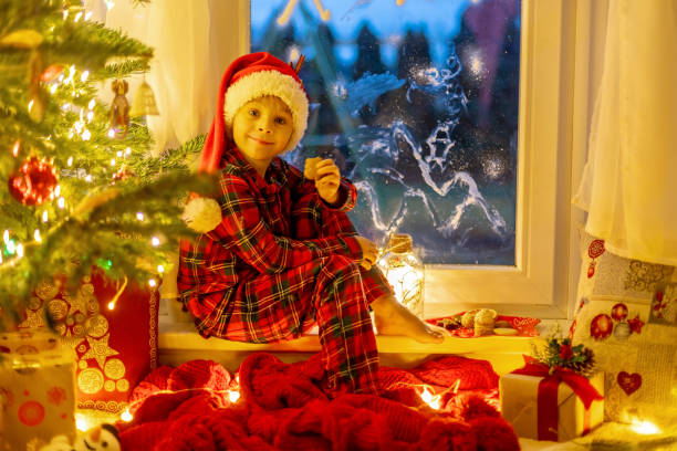 istock Cute child, sitting on a window, looking outdoors for Santa Claus 1962156938
