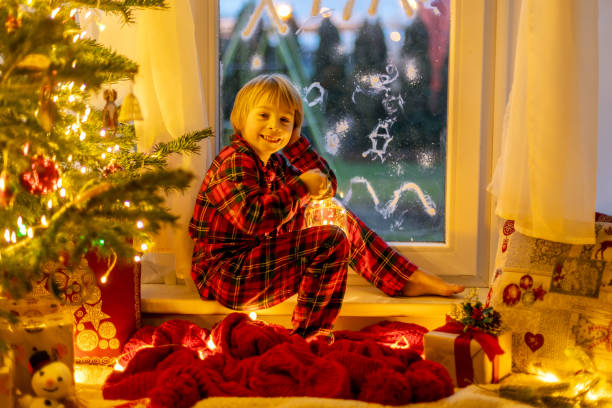 istock Cute child, sitting on a window, looking outdoors for Santa Claus 1962158423