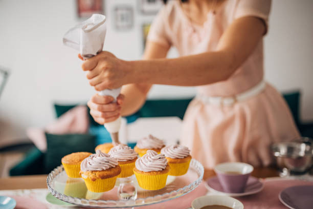 Classy young woman putting icing on muffins, preparing for her guests in her modern apartment.