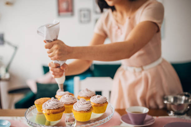 Classy young woman putting icing on muffins, preparing for her guests in her modern apartment.