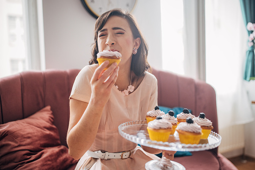Classy young woman eating homemade cupcake in her modern apartment.