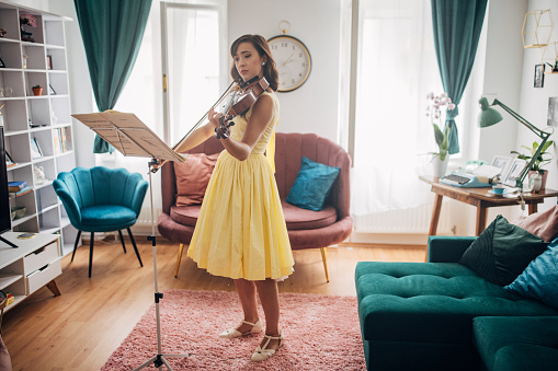 Classy young woman musician playing violin in her modern apartment.