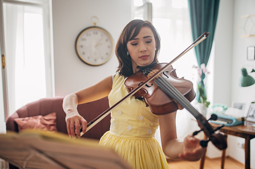 Classy young woman musician playing violin in her modern apartment.