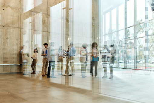 Large group of multi-tasking entrepreneurs working in a hallway of an office building. The view is through glass. Copy space.