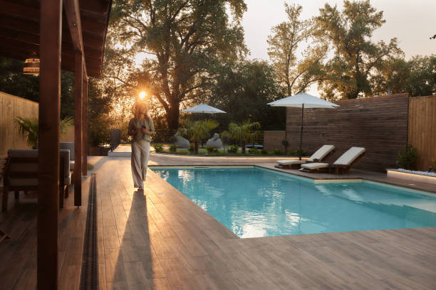 Happy woman using cell phone on the move by the pool at sunset.