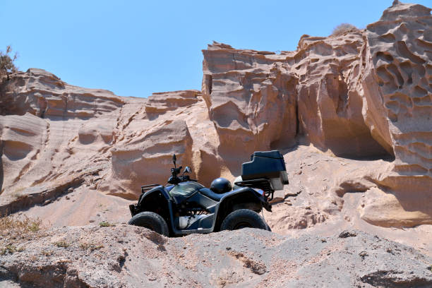 Quad bike parked on the seafront near the sandy beach of Monolithos on Santorini island, Greece. The coasts in this area resemble lunar-shaped landscapes. Travel, relaxation, adventure.