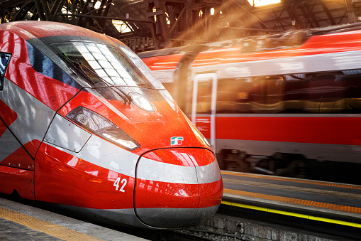Modern high-speed red trains in the morning sun at Milan Central Station, the main railway station of Milan in Italy and the largest railway station in Europe by volume