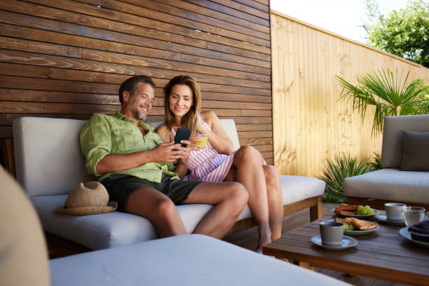 Happy couple using cell phone while relaxing on a patio.