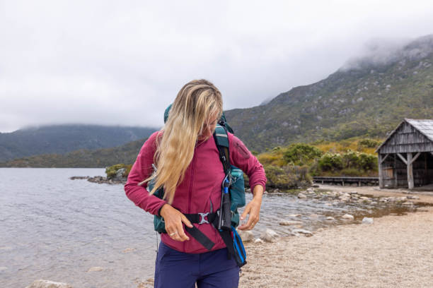 oasis de montaña: una mujer excursionista ajusta su mochila y se detiene junto al lago en medio de picos majestuosos - australian culture hiking australia people fotografías e imágenes de stock