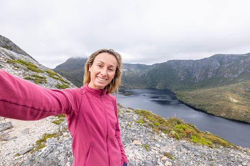 In the heart of Tasmania's wilderness, a young woman pauses during her trek to capture the essence of her journey. With a backdrop of breathtaking nature, she takes a selfie, immortalizing the spirit of exploration and discovery in the pristine landscapes.