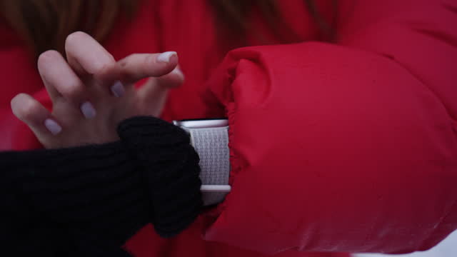 Close-up cropped shot of unrecognizable woman in red jacket using touching wearable smartwatch in city street. Closeup of female scrolling display on smart watch