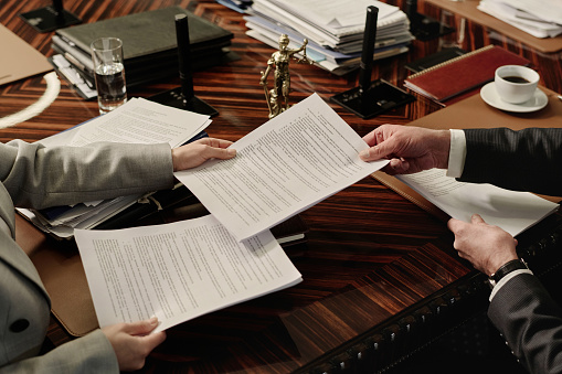 Closeup of hands of unrecognizable lawyers passing documents to each other over wooden desk