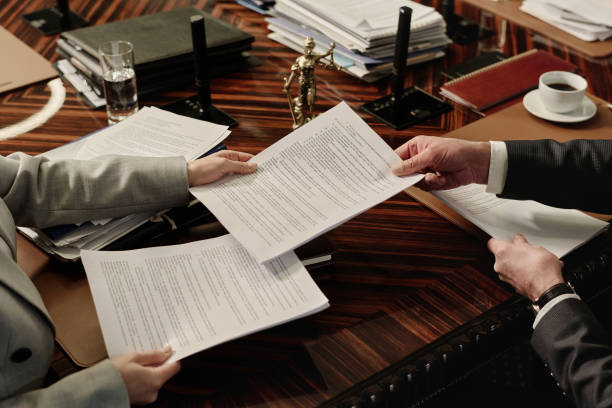 two attorneys exchanging documents sitting side by side at table - avukat stok fotoğraflar ve resimler