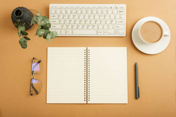 istock Desktop with blank notepad, keyboard, glasses and coffee cup on brown table. Top view, flat lay 1962307127