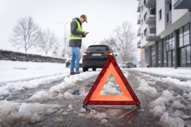 istock After vehicle breakdown, man using mobile phone to text, while warning triangle sign is on the road on winter cold weather 1962328401