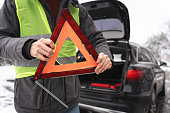 Unrecognizable man, assembling a warning triangle sign, during an vehicle breakdown on the road on winter cold weather