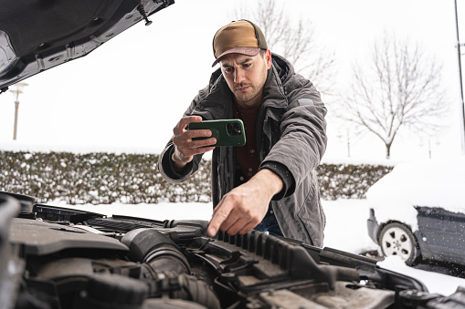 On the roadside, after an car breakdown, young Caucasian man taking with mobile phone photos of an car engine