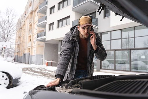 Young Caucasian man,talking on mobile phone with mechanic, while looking at the car engine, on the side of the street