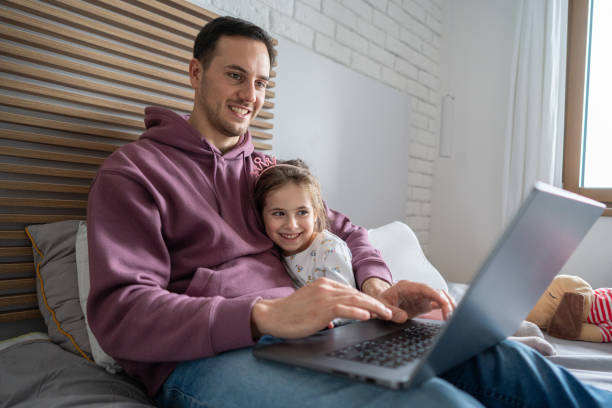 istock Young father working on laptop, while lying in the bed with his daughter 1962341225