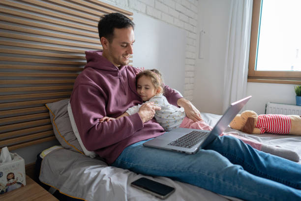 istock Father working on laptop, while lying in the bed with his daughter who hugs him 1962343358