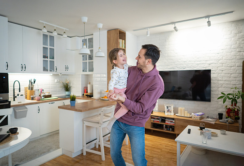 Young Caucasian man, an father dancing with his daughter in their modern home