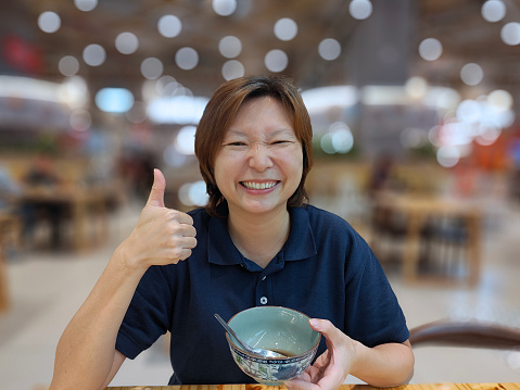 An Asian woman is giving a solid thumbs up after enjoying red bean dessert soup in restaurant