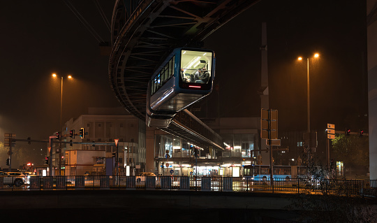 Schwebebahn - elevated suspension monorail cable car train, famous technological landmark and tourist attraction. Night cityscape of Wuppertal, North Rhine-Westphalia, Germany.