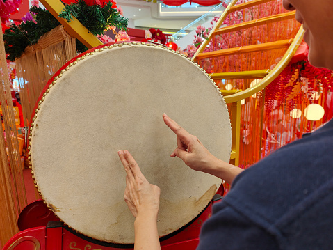 An Asian woman is enjoying classic drum instrument during Chinese New Year decorations in shopping mall