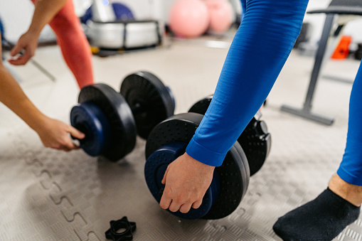 Young man and woman picking up dumbbells from the floor in the gym. Close-up.