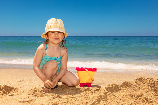 Happy little girl wearing panama hat enjoying a sunny day on a beach  playing with sand. Sun hat provide additional protection for child's face neck and ears