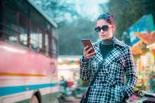 For a sustainable and eco-friendly lifestyle, a businesswoman prefers to go by public transport or walk while commuting after work within a 15-minute city of Himachal Pradesh. She read her phone to check the bus ticket and timing.