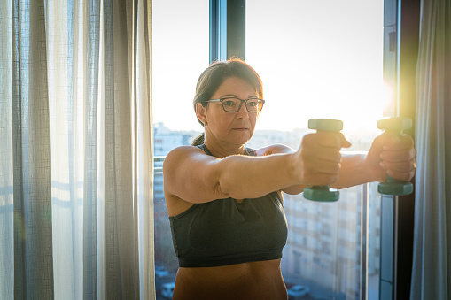 Portrait of mature woman with dumbbells doing exercise in the morning. High resolution 42Mp indoors digital capture taken with SONY A7rII and Zeiss Batis 25mm F2.0 lens