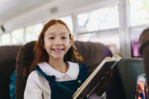 Portrait of a child girl reading a book on school bus