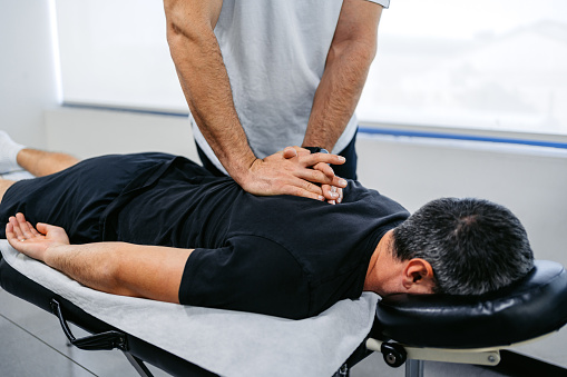 Chiropractor adjusting (cracking) his male client's upper back in his office.