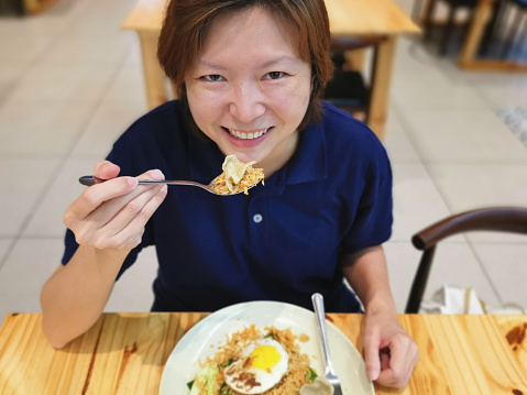 An Asian woman is enjoying local fried rice with fish crackers food in restaurant