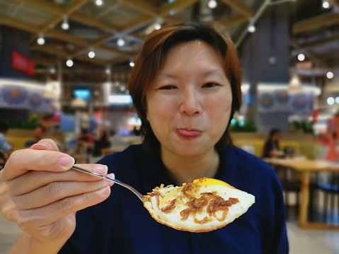 An Asian woman is enjoying sunny side up garnished with fried onion in restaurant
