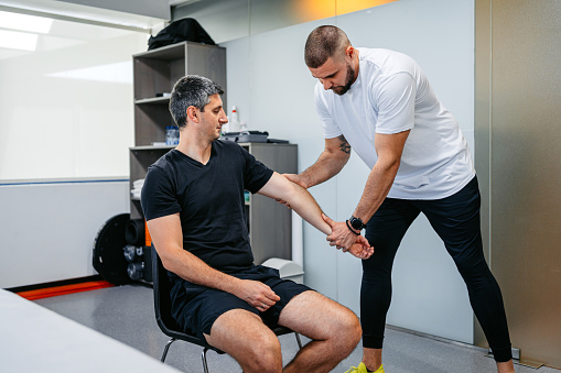 Physical therapist adjusting and massaging his male client's arm in his office.