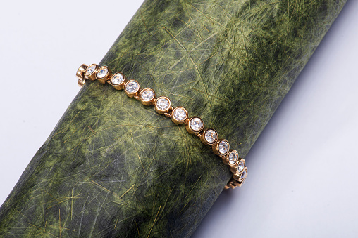 Studio shot close-up photo of a gold and diamond imitate on bracelet wrapped around a stylish hand made paper