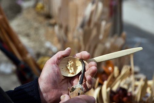 An engraver is carving a wooden spoon with a chisel on his hand with a traditional method. Process of making a carved wooden spoon.