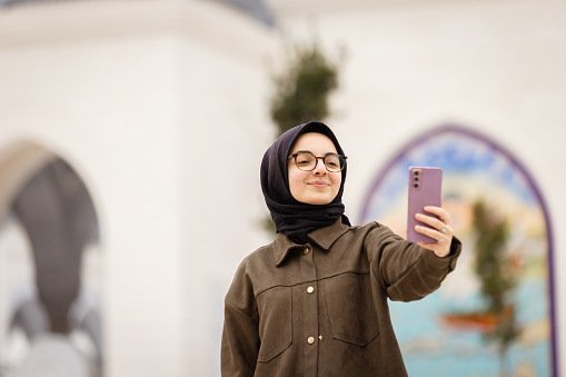 Young hijab lady is taking a selfie front of mosque.
Istanbul - Turkey.