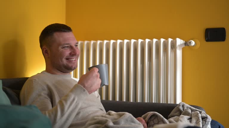 Smiling handsome man smiling while relaxing on sofa and drinking tea.