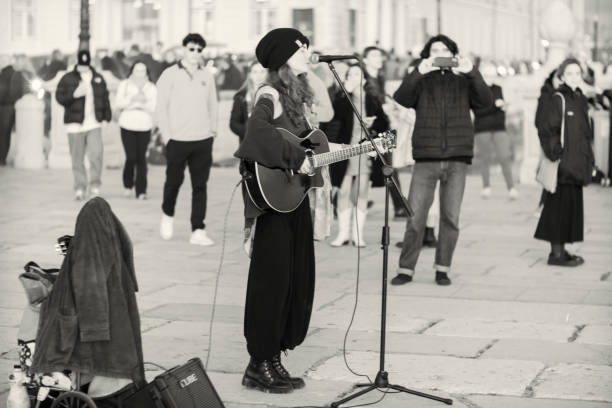 Lisbon, Portugal - December 17, 2022: A young female street musician plays a guitar and sings at the Praça do Comércio square in Lisbon downtown.