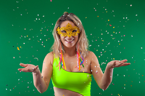 A cheerful woman, surrounded by a green backdrop, adorned in vibrant attire, joyfully releasing confetti into the air