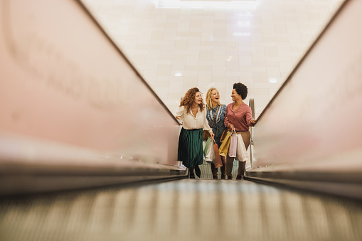 Shot of three cheerfu women having fun and standing on escalator in a city mall together while out on a shopping spree.