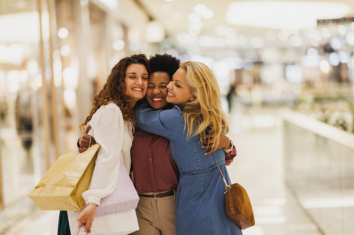 Cropped shot of three smiling girlfriends are hugging each other while taking some time out to enjoy a shopping spree in the city mall.