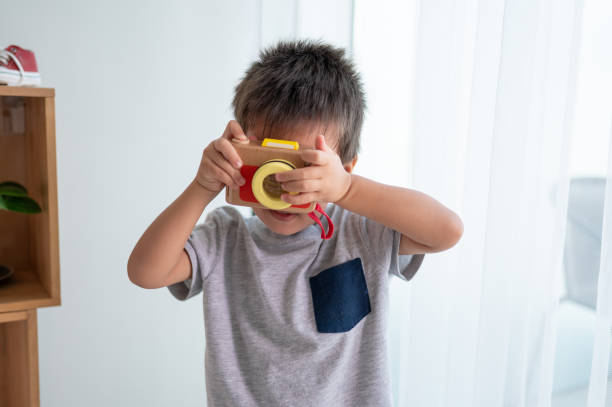 Two and a half years old baby boy having fun playing taking pictures with a small wooden toy camera. Imaginative play, creativity, learning and childhood development concepts