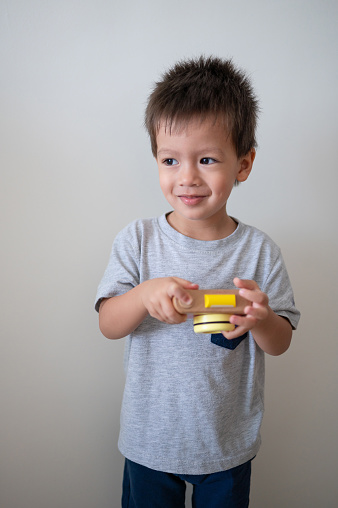 Two and a half years old baby boy having fun playing taking pictures with a small wooden toy camera. Imaginative play, creativity, learning and childhood development concepts